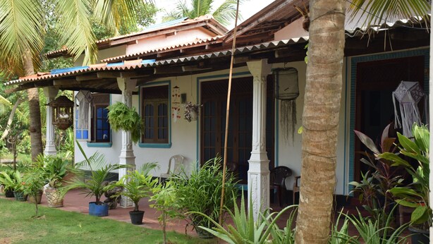 A traditional house with a tiled roof, white walls, and blue trim. There are several potted plants and a small garden area in front. - Little Guest (Anuradhapura)