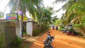 A rural road with a sign for rooms, a motorcycle, and a dirt path. - Little Guest (Anuradhapura)