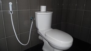 A toilet with a bidet attachment in a tiled bathroom. - Little Guest (Anuradhapura)