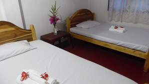 A room with two wooden beds, each with white bedding and pillows. There is a small wooden nightstand with a vase of flowers between the beds. - Little Guest (Anuradhapura)
