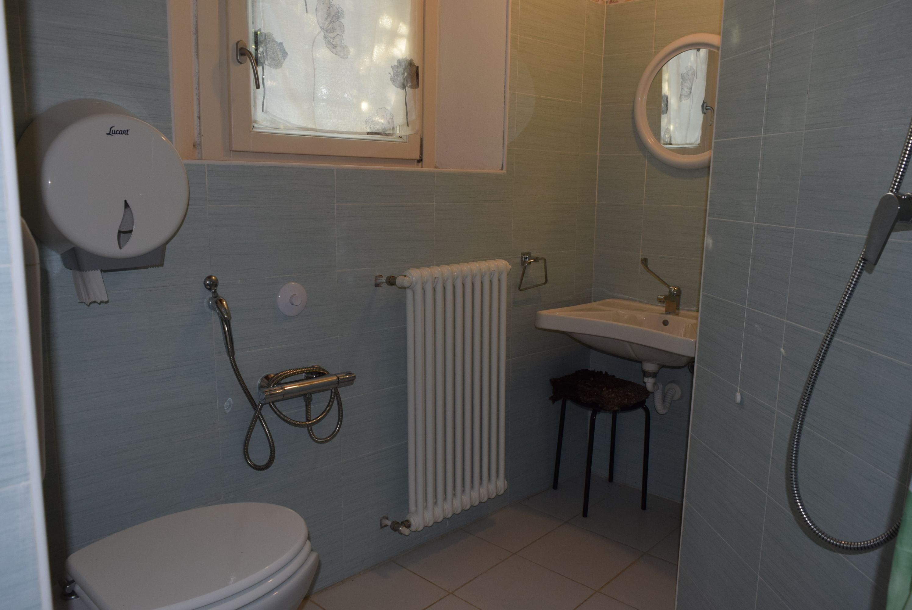 A bathroom with a toilet, a sink, a shower, and a window with a flower decoration.