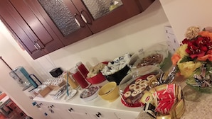 Eine Küchenarbeitsfläche mit verschiedenen Lebensmitteln und Küchenutensilien, darunter eine Obstschale, ein Glas Saft und eine Schüssel mit Müsli.