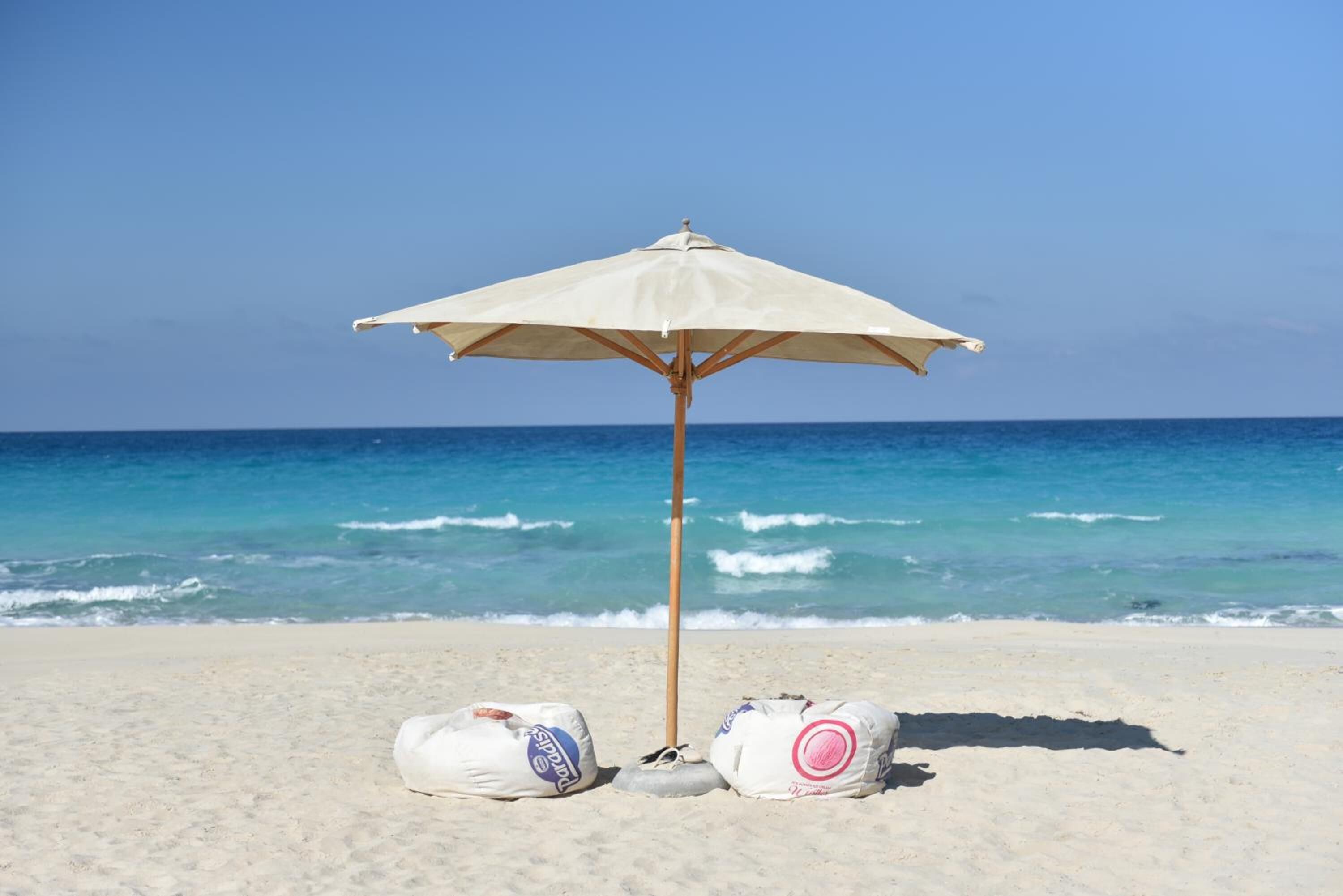 Ein Strandsonnenschirm mit zwei Taschen im Sand.