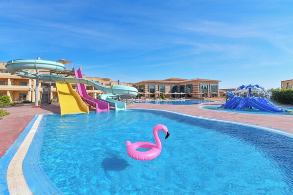 A swimming pool with a pink flamingo float, a water slide, and a blue water feature.