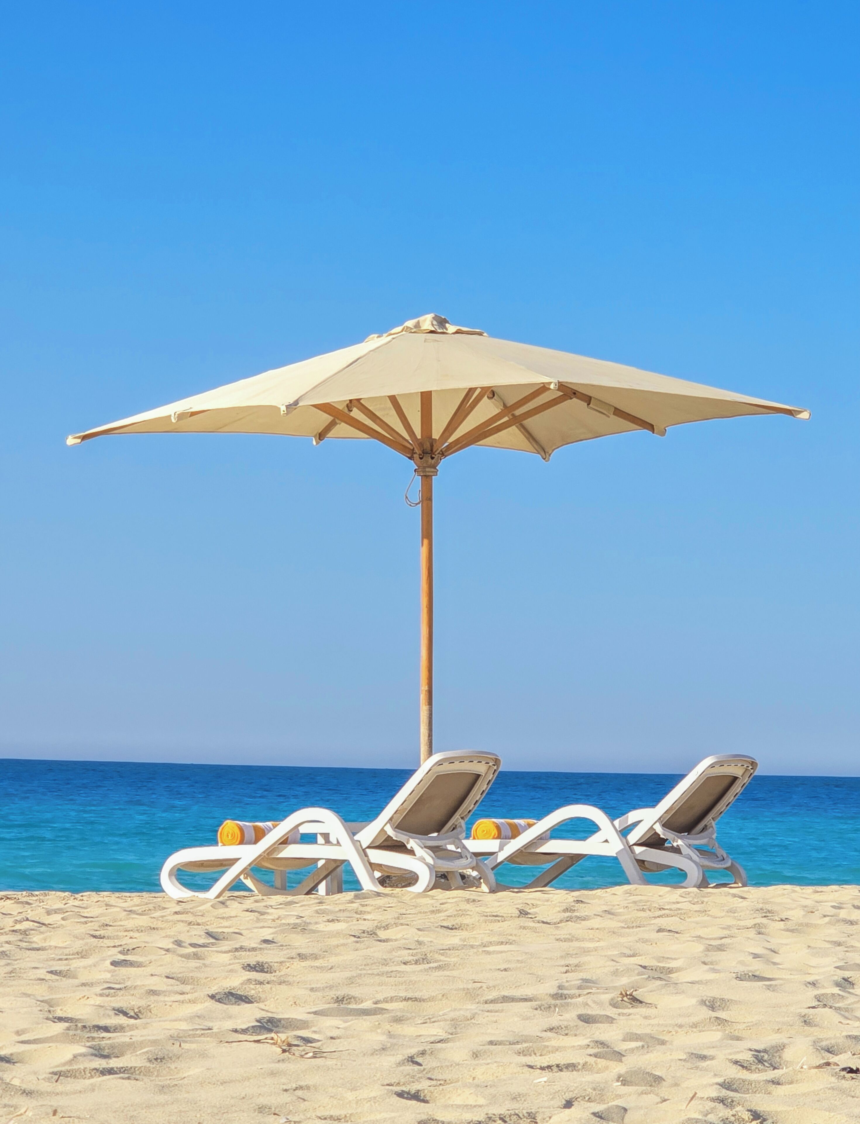 Une scène de plage avec un grand parasol, trois chaises longues et l’océan en arrière-plan.
