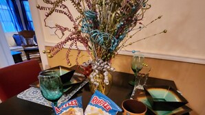 Een eettafel met een vaas gedroogde planten, een mand met snacks en een mok.
