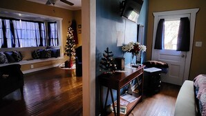Een woonkamer met een houten vloer, een plafondventilator, een kerstboom, een aan de muur bevestigde televisie en een deur met een raam.