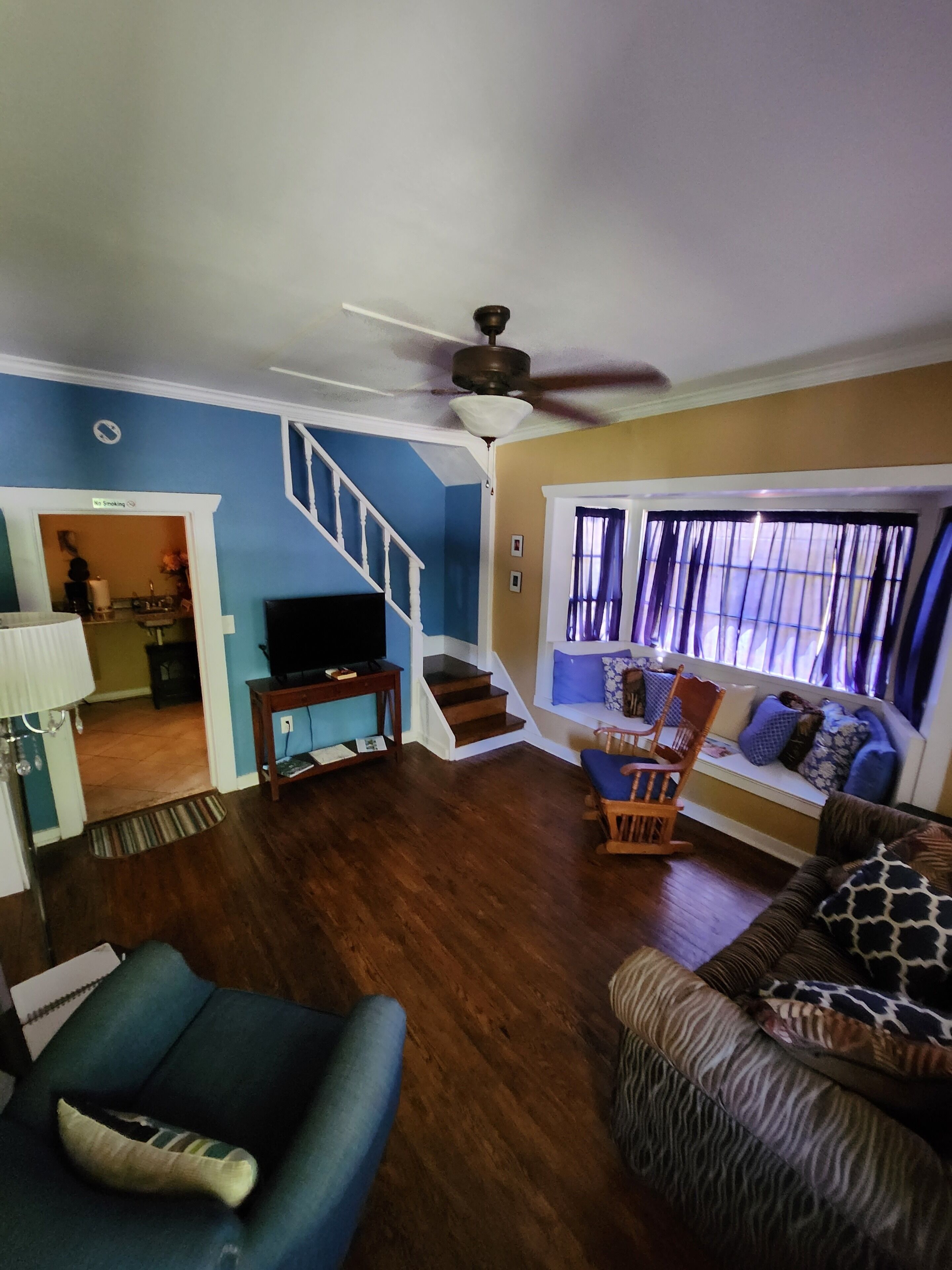 A living room with a sofa, a chair, a television, a staircase, and a ceiling fan.