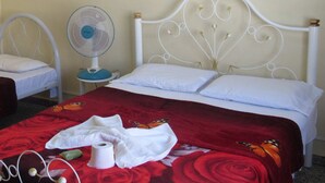 Una camera da letto con un letto, un comodino, una ventola a muro e una coperta a fiori rossi.