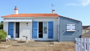 Una casa a due piani con tetto in tegole rosse, persiane blu e un piccolo patio con tavolo e sedie.
