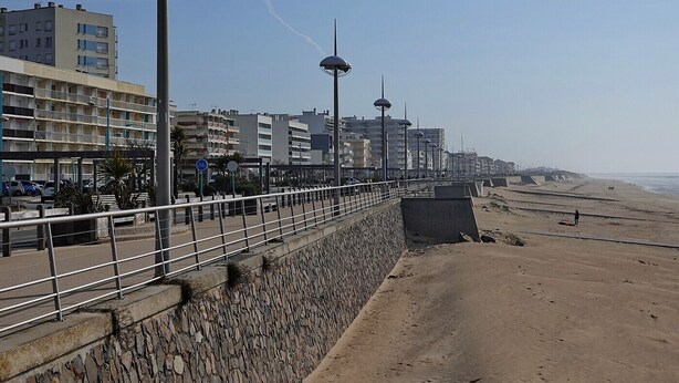 Una passeggiata costiera con un muro in pietra, ringhiera in metallo e moderni edifici sullo sfondo.