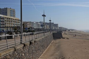 A coastal promenade with a stone wall, metal railing, and modern buildings in the background.