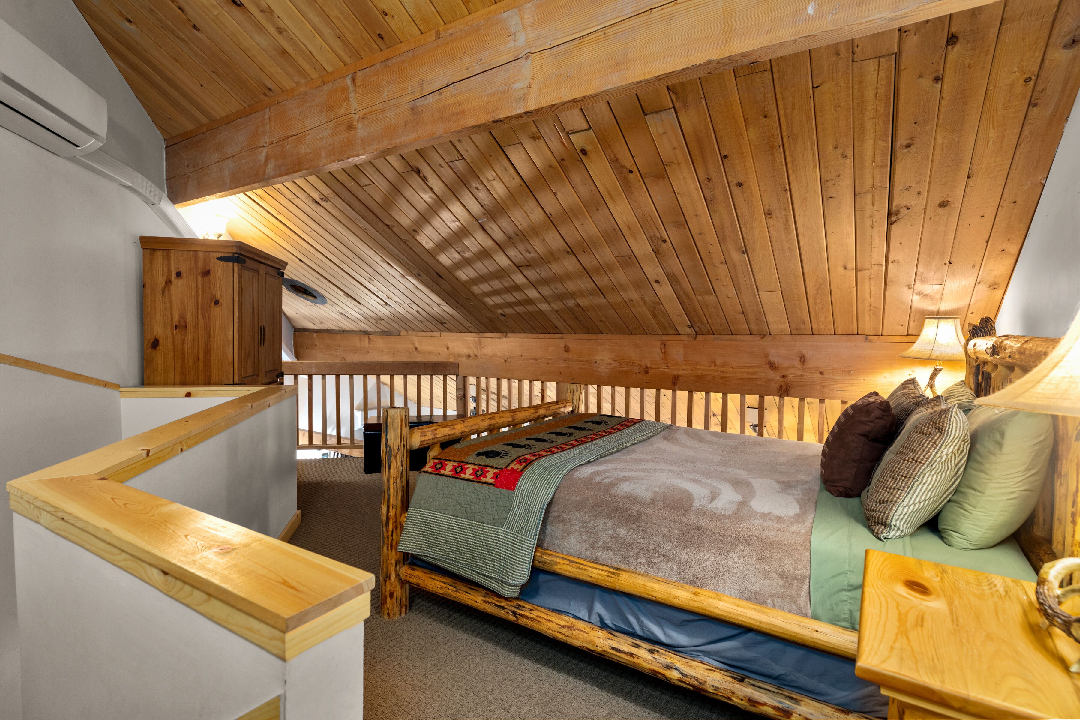 Un dormitorio estilo loft con techo inclinado, estructura de cama de madera, mesita de noche, lámpara y armario de madera.