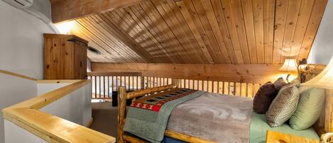 Un dormitorio estilo loft con techo inclinado, estructura de cama de madera, mesita de noche, lámpara y armario de madera.