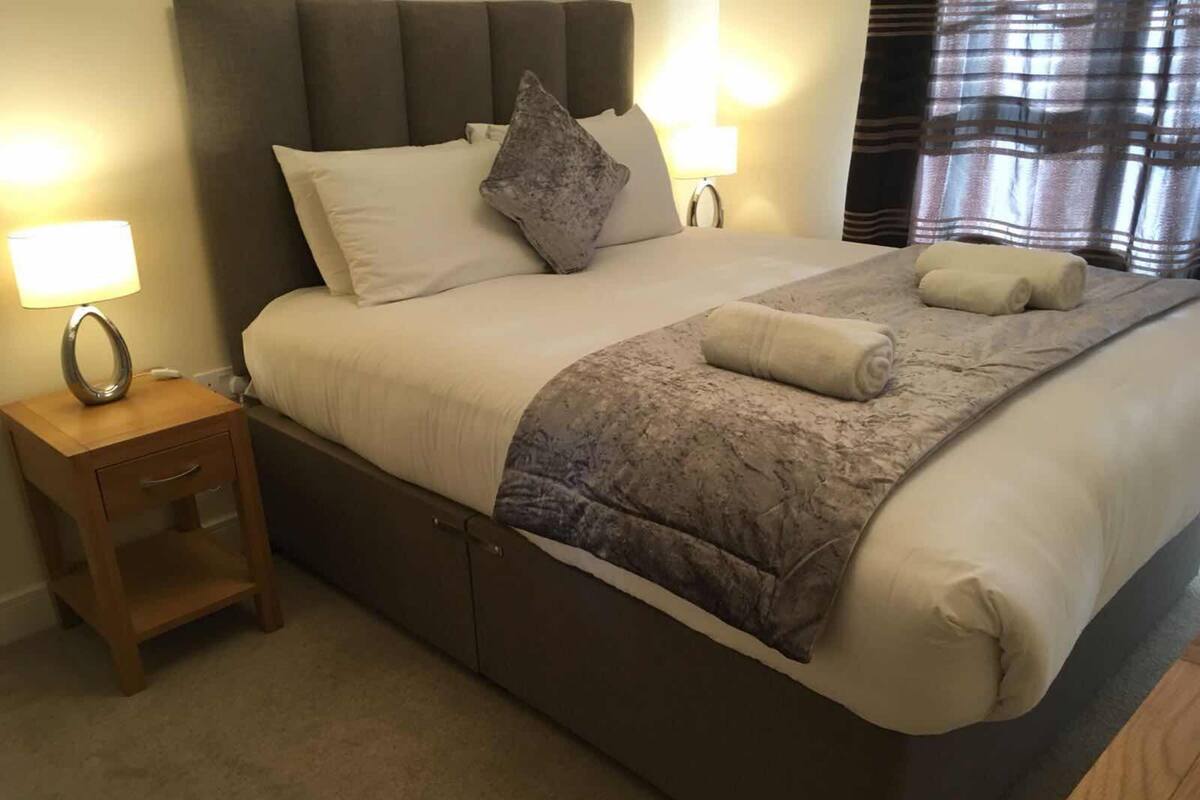 A neatly made bed with a grey headboard, two bedside lamps, and a wooden nightstand with a lamp.