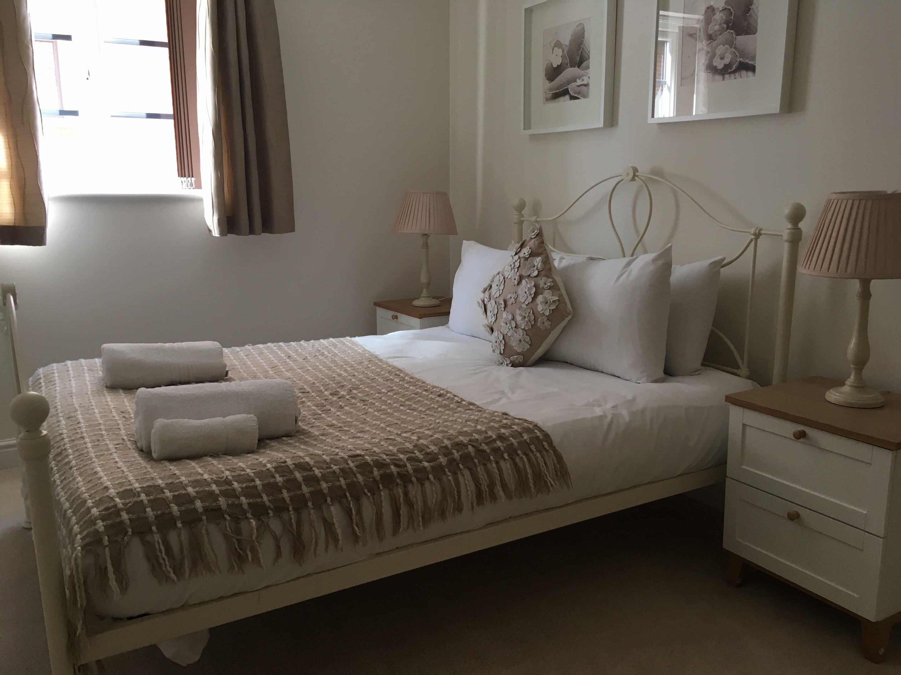 A neatly made bed with towels, a bedside table with a lamp, and a wall with framed pictures.