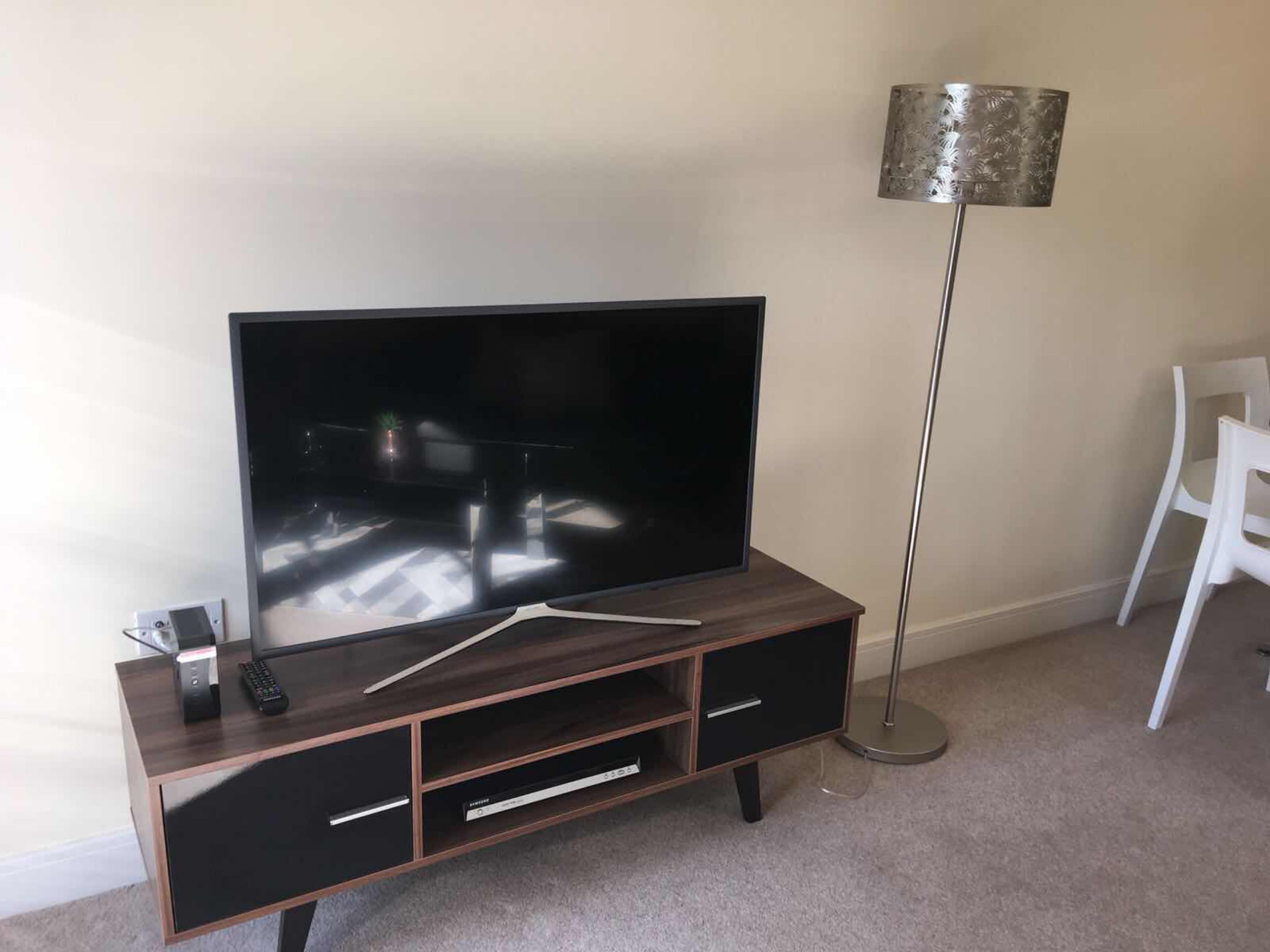 A modern living room with a flat-screen TV on a wooden TV stand, a floor lamp, and a white chair.