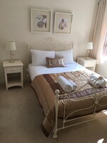 Un dormitorio ordenado con una cama, dos mesitas de noche y dos cuadros colgados en la pared.