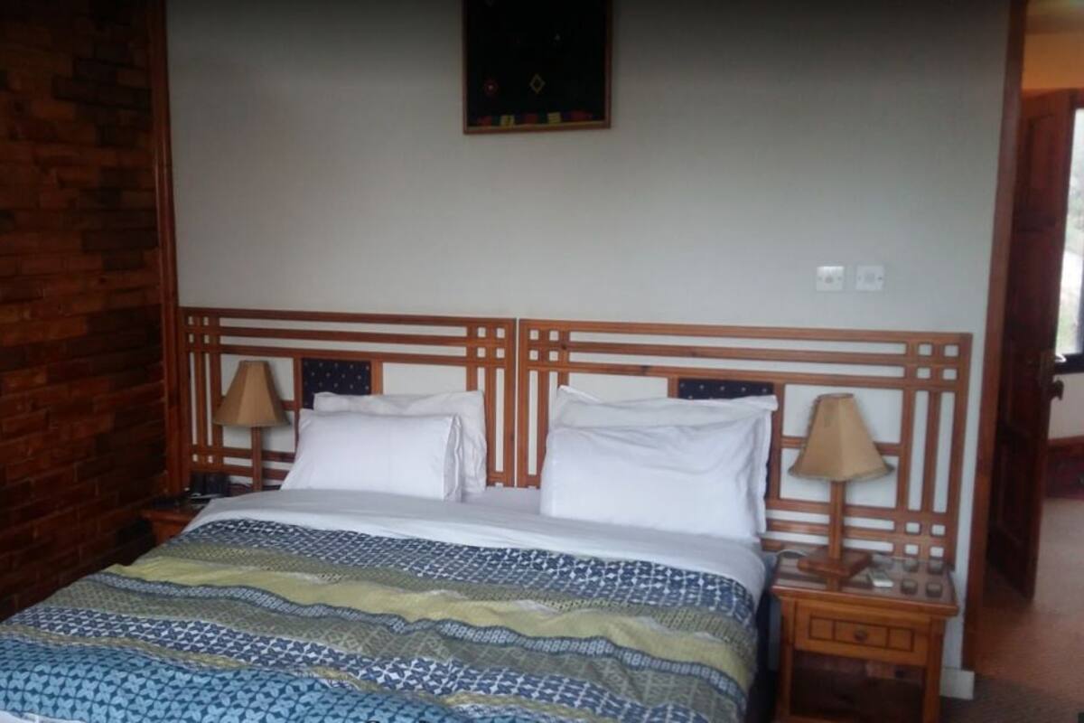 Quarto com cabeceira de madeira, colcha estampada, duas mesas de cabeceira com luminárias e parede de tijolos.