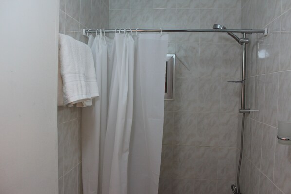 A shower area with a glass door, a metal showerhead, and a towel rack with multiple towels. - Rafiki Hostel (Wadi Musa)