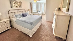A bedroom with a bed, a dresser, a ceiling fan, and a window with curtains. - House on the 16th Tee! (Howard)