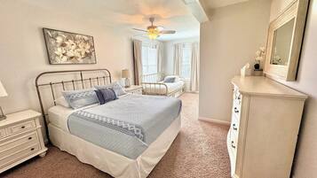 Une chambre à coucher avec un lit, une commode, un ventilateur de plafond et une fenêtre avec des rideaux.