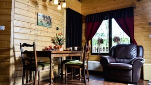 Ein gemütliches Blockhaus-Interieur mit Holzwänden, einem Esstisch mit Stühlen, einem Ledersessel und einem Fenster mit Vorhängen.