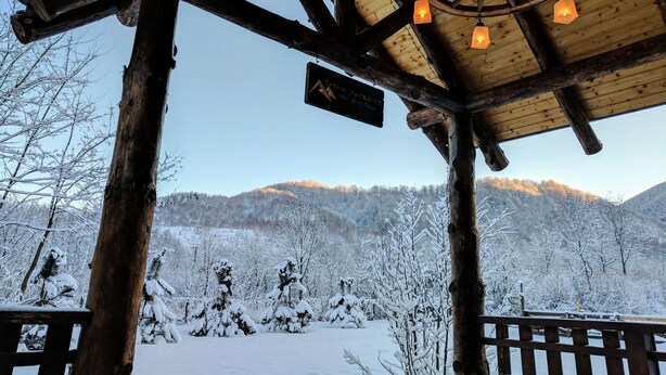 Eine Holzhütte vor einer verschneiten Landschaft und Bergen im Hintergrund.