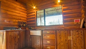A wooden cabin interior with a kitchen area, including a stove, sink, and cabinets. - Triple Tui - Log cabin, self contained, river side (Murchison)