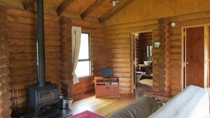 A log cabin interior with a fireplace, wooden furniture, and a cozy living area. - Triple Tui - Log cabin, self contained, river side (Murchison)