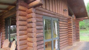 A log cabin with a porch, large windows, and wooden chairs. - Triple Tui - Log cabin, self contained, river side (Murchison)