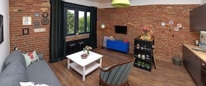 Cozy seating area with a sofa and dining table, small kitchen with sink and countertop, and a TV mounted on the wall.
