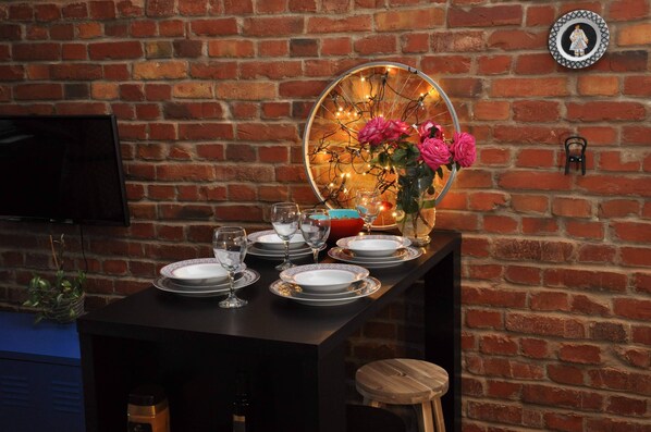 A dining area with a round mirror and table set for a meal, featuring a vase with flowers and a television on the wall.