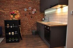 Compact kitchen with a brick wall backdrop, sink, stove, oven, and shelving unit for storage.