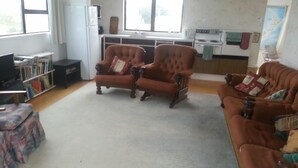 Een woonkamer met een bank, fauteuils, een boekenkast, een televisie en een keuken op de achtergrond.