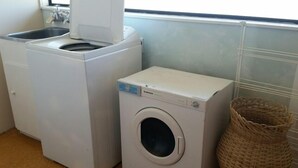 Een wasruimte met een voorlader wasmachine en droger, een rieten mand en een raam met zonwering.
