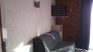 Une pièce avec un canapé, un téléviseur fixé au mur et une fenêtre avec des rideaux.