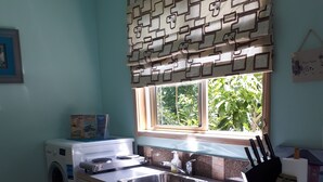 Eine kleine Küche mit Waschmaschine, Spüle und einem Fenster mit gemusterten Vorhängen.