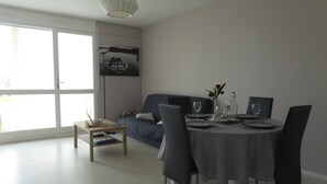 Ein Essbereich mit einem runden Tisch für zwei Personen, einer Couch und einem großen Fenster.