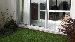 Ein modernes Gebäude mit großen Schiebeglastüren, einer kleinen Terrasse mit Holztisch und Stuhl sowie einem gepflegten Rasen.