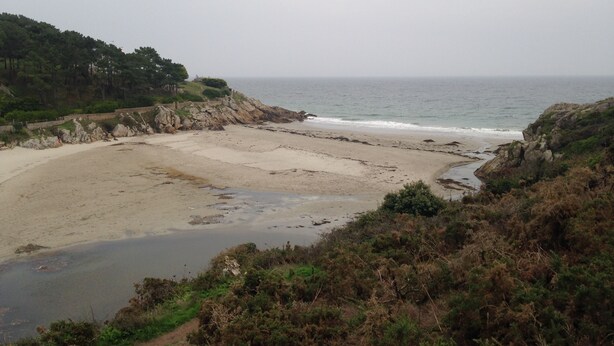 Ein Küstenstrand mit felsigem Gelände und freiem Blick auf das Meer.