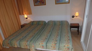 Een kamer met een bed, twee wandlampen, een kleine tafel en een prullenbak.