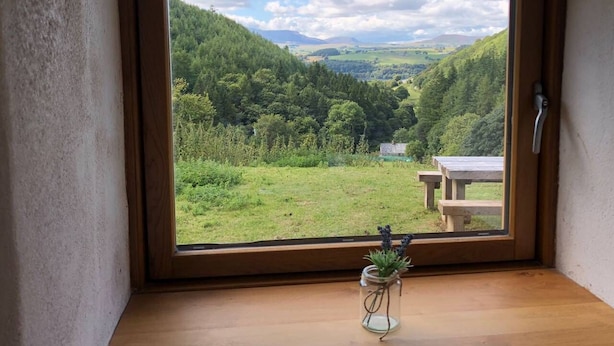 Une pièce dotée d’une grande fenêtre donnant sur une vallée verdoyante et des montagnes lointaines.