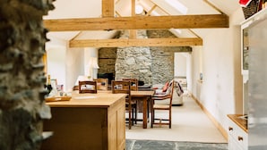 Un intérieur rustique avec des poutres apparentes, une cheminée en pierre, une table à manger en bois et un coin salon confortable.