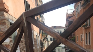 Un gato descansando sobre una terraza de madera con vista a un canal y edificios al fondo.
