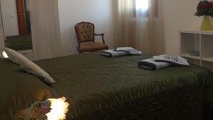 Un dormitorio con cama, una silla, una mesita de noche, una lámpara y una ventana con cortinas.