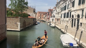 Un canal estrecho con barcos, edificios a ambos lados y una persona remando.