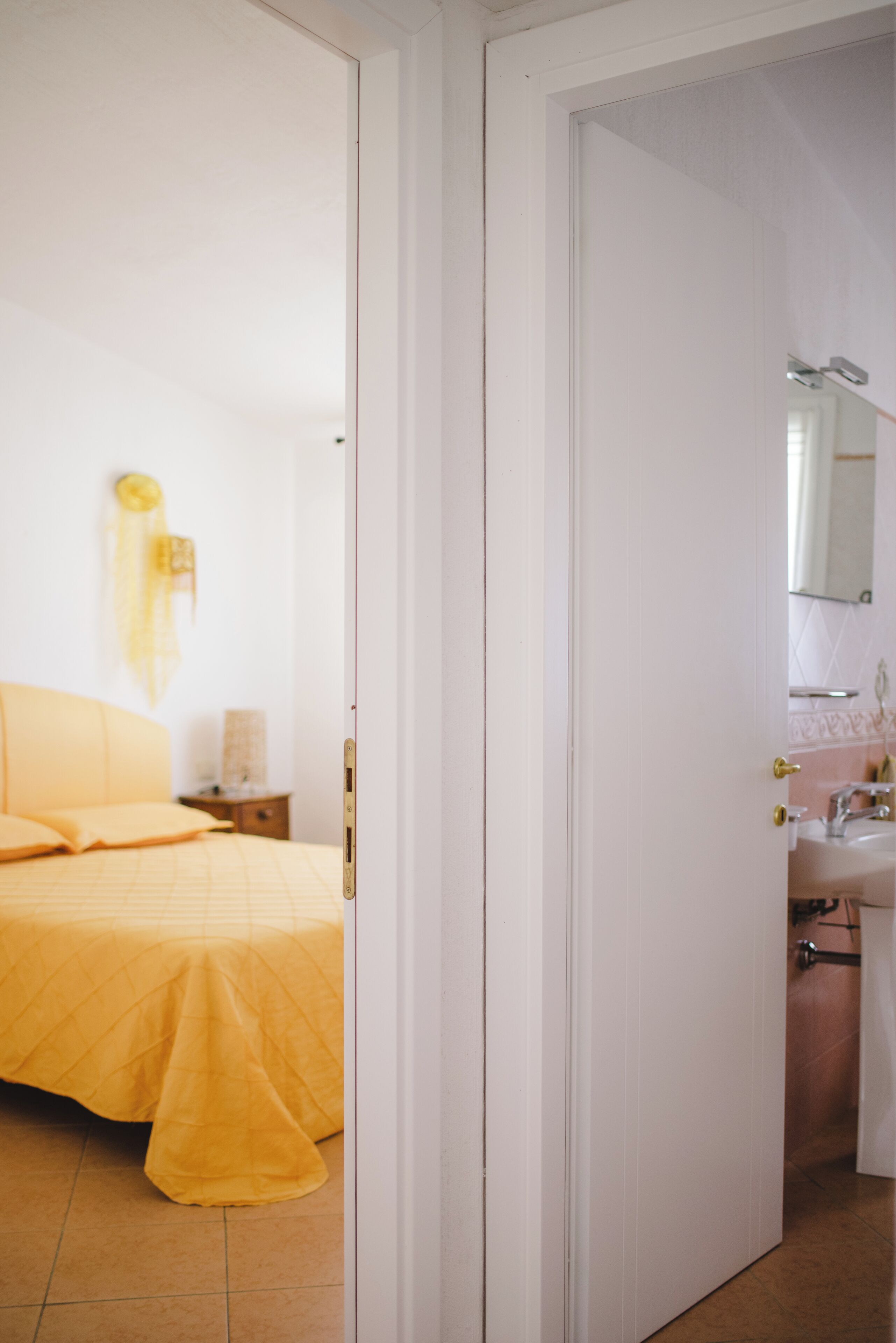 A bedroom with a bed, bedside table, and a bathroom with a sink and mirror.