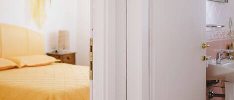 A bedroom with a bed, bedside table, and a bathroom with a sink and mirror.