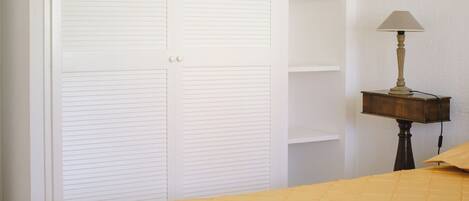 A bedroom with a large white wardrobe, a bedside table with a lamp, and a yellow bedspread.